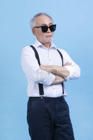 joven activo senior coreano asiático masculino usando gafas de sol contra fondo de estudio