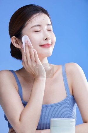 beauty concept photo of korean asain beautiful woman holding cleansing pads alongside a product, studio background