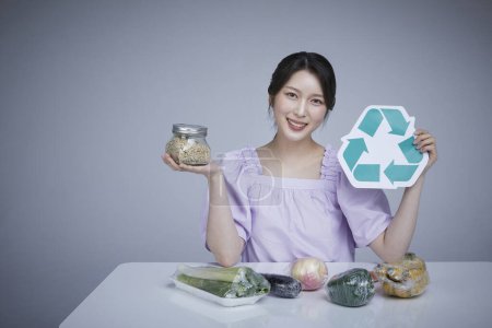 Zero Waste, Obst und Gemüse in Einwegverpackung mit Recycling-Etikett Bild einer Koreanerin, die Mehrkornreis in einem Glas isst.