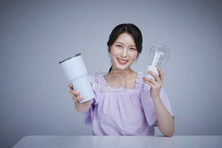 Koreanisch als schöne Frau mit einem Zero-Waste-Tumbler und einem Einweg-Plastikbecher.