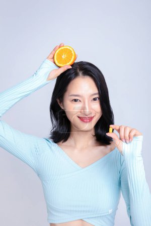 Una mujer sosteniendo una pastilla y una naranja