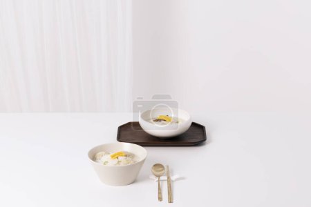 Two bowls of rice cake soup and a spoon are placed on a white table