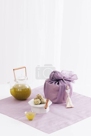 Hay teteras, tazas de té y pasteles de arroz alrededor del regalo envuelto en tela