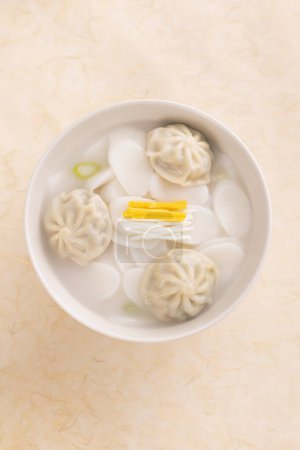 On top of Korean paper, there's a white bowl of rice cake dumpling soup