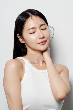 una mujer asiática que cierra los ojos suavemente y se cubre el cuello con una mano
