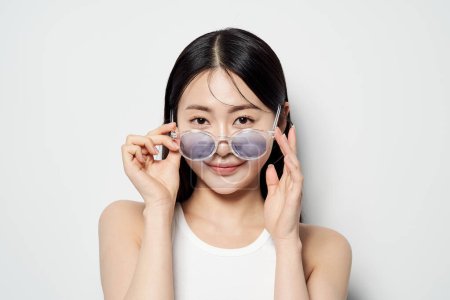 Asian woman staring straight ahead with transparent sunglasses down with both hands