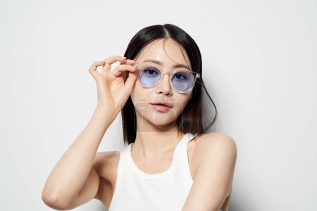 Asian woman staring straight ahead wearing transparent sunglasses with one hand