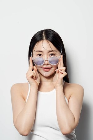 une femme asiatique portant des lunettes de soleil avec les deux mains et souriant