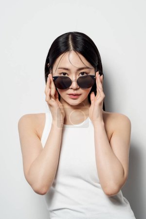 Asian woman staring straight ahead with her sunglasses slightly down with both hands