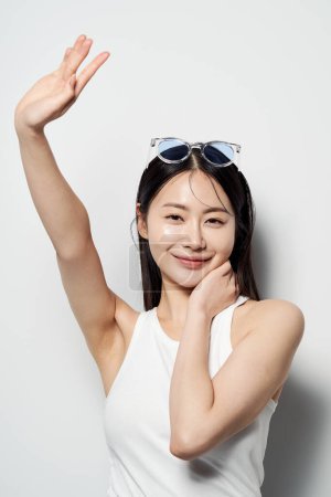 eine Asiatin, die mit erhobenen Händen und Sonnenbrille lächelt