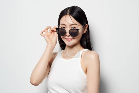 an Asian woman who pulls down her sunglasses with one hand