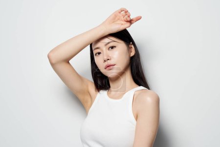 Asian woman posing with her hand on her head against a white background
