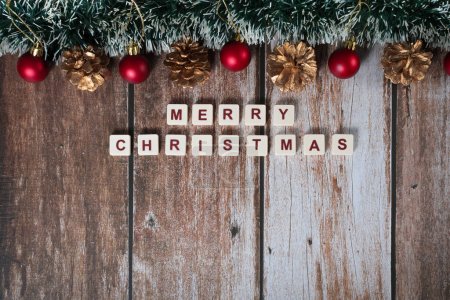 Photo for Merry Christmas written with letters of a game and Christmas ornaments on a wooden background - Royalty Free Image