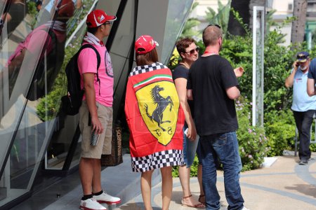 Foto de Fontvieille, Mónaco - 28 de mayo de 2016: Pareja joven, ambos fans de la Scuderia Ferrari, con gorras Ferrari y la chica envuelta en una bandera Ferrari, durante el Gran Premio de Mónaco en Montecarlo - Imagen libre de derechos