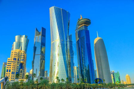Foto de Doha, Qatar - 20 de febrero de 2019: Complejo Al Fardan Towers y Doha Tower, emblemáticos rascacielos acristalados en West Bay. Rascacielos del Distrito Financiero en Oriente Medio. Cielo azul soleado. - Imagen libre de derechos