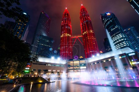Foto de Kuala Lumpur, Malasia - Enero 2023: Al caer la noche, las Torres Gemelas Petronas crean un contorno impresionante contra el cielo oscurecido, sus fuentes iluminadas comienzan a brillar y moverse.. - Imagen libre de derechos