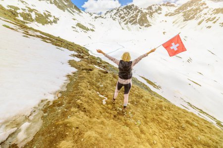 Téléchargez les photos : Femme touristique à avec drapeau suisse dans la neige sur le mont Muottas Muragl de la Suisse. Excursions populaires en montagne dans le canton de Graubunden en Suisse. - en image libre de droit