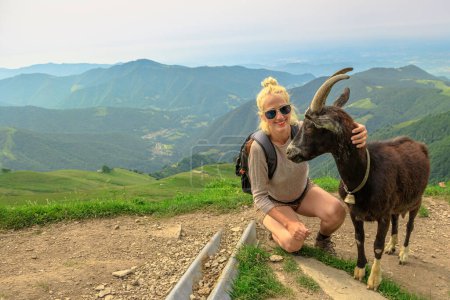 Photo for Backpacker tourist Woman playing with a goat in Monte Generoso peak. Top of Mendrisio district of Switzerland in ticino canton. - Royalty Free Image