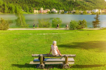 Tourist lady sitting in the park of St. Moritz by Lake St. Moritz in Switzerland. St. Moritz lakefront in Grisons Canton in Maloja region.