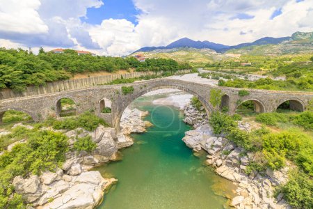 Téléchargez les photos : Mesi Bridge en Albanie est une merveille architecturale époustouflante qui enjambe la rivière Kir dans un village pittoresque. Ce pont historique en pierre, originaire de l'époque ottomane, apporte un sentiment de patrimoine à l'environnement. - en image libre de droit