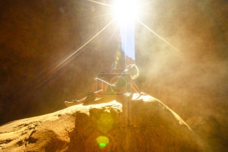 Foto de Mujer turista sentada en una roca con efectos de luz solar con arena volando en el desfiladero natural de Standley Chasm, West MacDonnell Ranges. Australian outback Red Center, Territorio del Norte, Australia. - Imagen libre de derechos