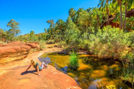 Tourist woman relaxing after trekking along Arankaia Walk in the heart of Palm Valley Oasis waterhole, Finke Gorge National Park. Tourism in Australian Outback, Northern Territory, Central Australia
