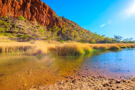 Téléchargez les photos : Glen Helen Gorge avec des rayons de soleil et un trou d'eau dans l'arrière-pays d'Australie centrale. Formation rocheuse West MacDonnell Ranges National Park dans le Territoire du Nord le long de Red Center Way
. - en image libre de droit