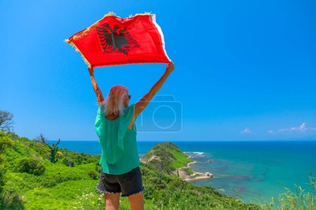 Foto de Mujer con bandera albanesa en Cabo de Rodon en Albania. Las tranquilas playas a lo largo del cabo ofrecen oportunidades para relajarse, nadar y tomar el sol.. - Imagen libre de derechos