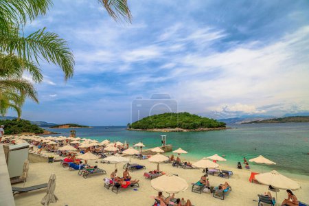 Photo for Ksamil , Albania - June 9, 2023: People sunbathing on the soft sandy shores of Ksamil Beach, where the sparkling turquoise waters beckon them to venture into the sea and explore the islands. - Royalty Free Image