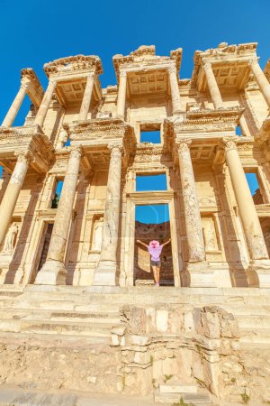 Foto de Una turista se encuentra asombrada ante la grandeza de la Biblioteca de Celso en Éfeso, Turquía, sus ojos trazando los intrincados detalles de la antigua fachada bañada por la suave luz del sol - Imagen libre de derechos