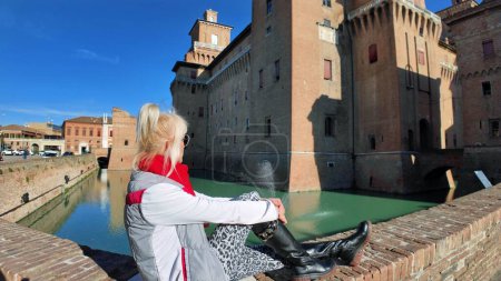 Photo for Tourist woman visiting the Ferrara castle of Italy. Surrounded by wide moat filled with water, which gives it a sense of isolation and protection. The castle has a square shape with 4 massive towers. - Royalty Free Image