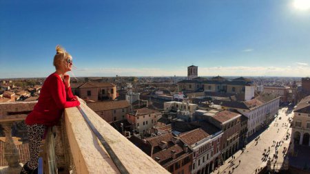 Photo for Tourist woman visiting Ferrara Castle climbed spiral staircase of Lions Tower and reached top of Estense fortress, gazing at the stunning view of the city, with its red roofs and ancient churches. - Royalty Free Image