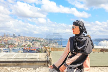 From Suleymaniye Mosque, Islamic woman in traditional Arab hijab dress takes in breathtaking panorama of Istanbuls skyline. Grand mosque, commissioned by Suleiman the Magnificent in 1500s in Turkey.