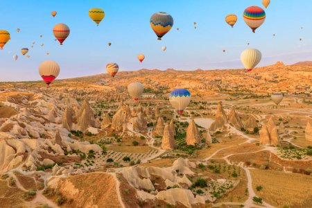 With their vibrant hues, hot air balloons ascend Cappadocian sky at dawn. Shed an enchanting glow on the distinctive summits beneath them in Goreme Rose Valley, a region of Cappadocia in Turkey.