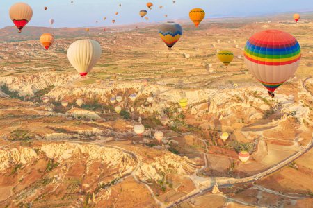 At dawn, a multitude of Cappadocias vibrant air balloons ascend gracefully, casting a surreal spectacle against the tranquil Rose Valley of Goreme in Turkey