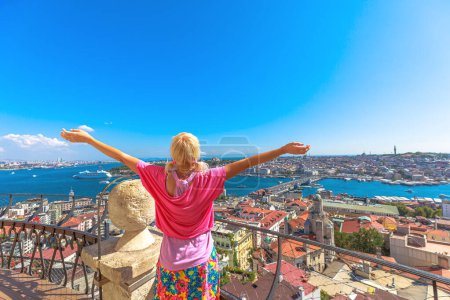 Rückansicht einer Frau mit offenen Armen, die das panoramische Stadtbild von Istanbul von einem hohen Aussichtspunkt an einem sonnigen Tag in Istanbul genießt