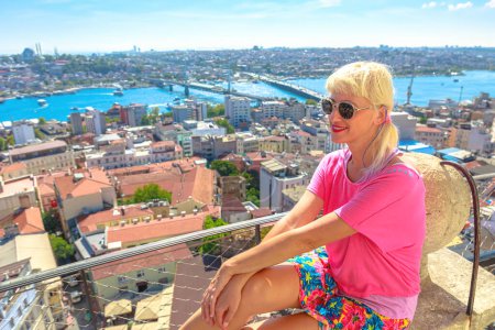 Woman gazes out at a vibrant cityscape from a high vantage point on a sunny day from the Galata Tower of Istanbul in Turkiye.