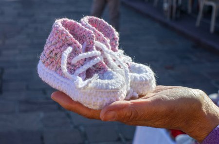 Téléchargez les photos : Chaussons de bébé faits à la main gros plan. Main avec chaussons au crochet pour bébé. Photo de haute qualité - en image libre de droit