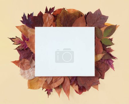 Foto de Hojas de otoño y lienzo blanco sobre fondo amarillo con espacio para copiar. Composición plana horizontal mínima, concepto de belleza otoñal - Imagen libre de derechos