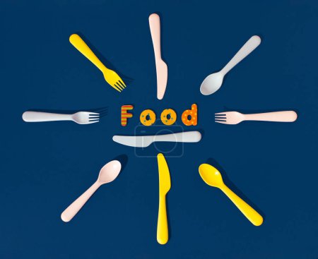 Foto de Set of plastic spoons, knives, forks and word food on a blue background. Minimal horizontal flat lay composition, funny fast food serving concept - Imagen libre de derechos