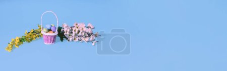 Foto de Easter eggs in basket and spring tree branches on bkue gray background. Minimal horizontal composition, banner with copy space, spring and Easter decoration concept - Imagen libre de derechos
