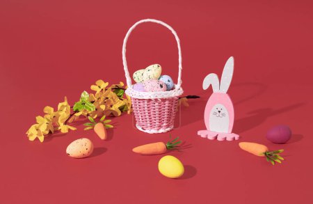 Foto de Conejo de Pascua, huevos en cesta, zanahorias y rama de árbol de primavera sobre fondo rojo. Composición horizontal mínima, concepto de decoración de Pascua - Imagen libre de derechos