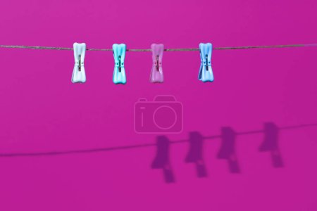 Foto de Pinzas de ropa en la cuerda con sombra sobre un fondo púrpura. Composición horizontal mínima, concepto de belleza de colores - Imagen libre de derechos