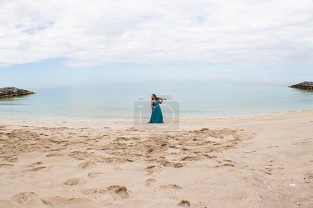 Violinist plays on the sandy beach. Musicant. Music. Musical performerA violinist plays on a sandy beach in a long dress. Asian woman with long hair plays the violin on the beach