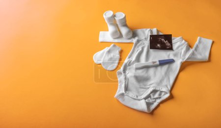 Foto de Prueba de embarazo positiva en el fondo de la ropa infantil. Hay espacio para el texto. - Imagen libre de derechos