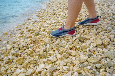 Männerfüße in Aquashoes stehen auf kleinen Steinen.