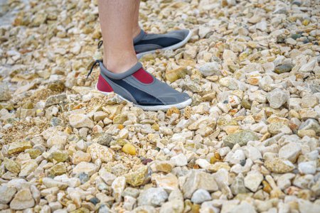 Téléchargez les photos : Les pieds des hommes dans les aquashoes se tiennent sur de petites pierres. - en image libre de droit