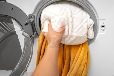 Una mano empuja una almohada en la lavadora. Lavado de artículos grandes.