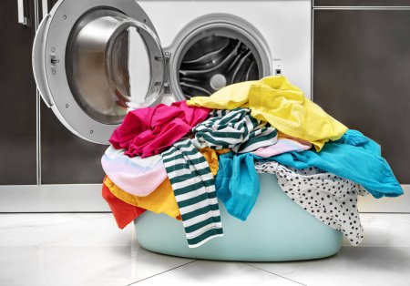 Téléchargez les photos : Blanchisserie multicolore pour le lavage dans la machine à laver se trouve dans le panier. - en image libre de droit