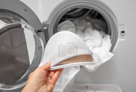 Foto de Una mano pone ropa interior de mujer en la lavadora. Primer plano. - Imagen libre de derechos